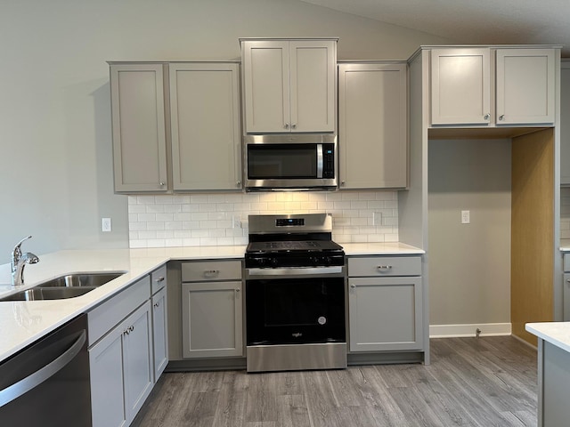 kitchen with light wood-type flooring, stainless steel appliances, vaulted ceiling, sink, and gray cabinets