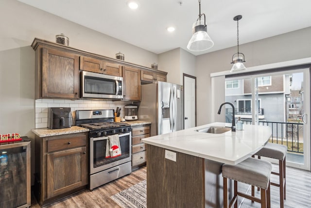 kitchen with a center island with sink, sink, a wealth of natural light, appliances with stainless steel finishes, and decorative light fixtures