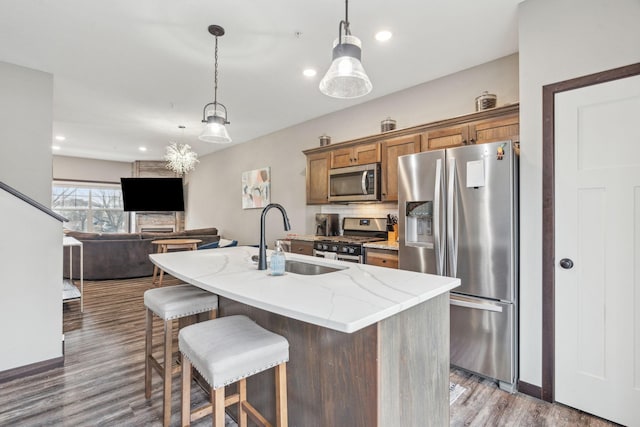 kitchen featuring light stone counters, sink, stainless steel appliances, and decorative light fixtures