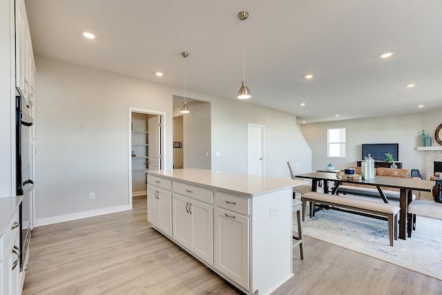 kitchen featuring decorative light fixtures, white cabinetry, a kitchen island, and light hardwood / wood-style floors