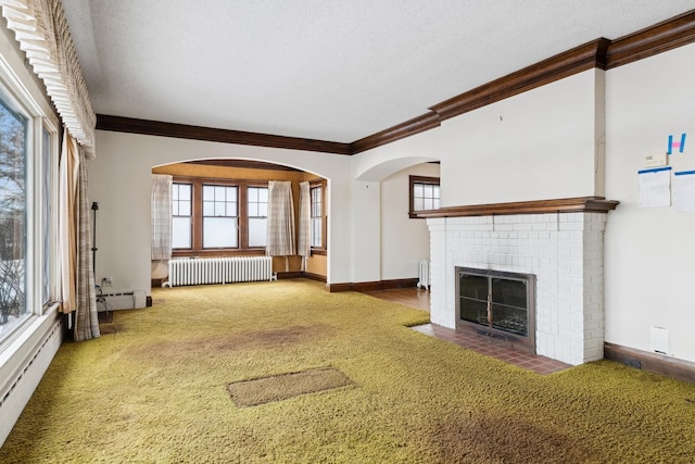 unfurnished living room featuring carpet floors, a brick fireplace, a wealth of natural light, and radiator heating unit