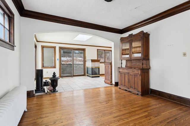 unfurnished living room with radiator, ornamental molding, a textured ceiling, and light wood-type flooring