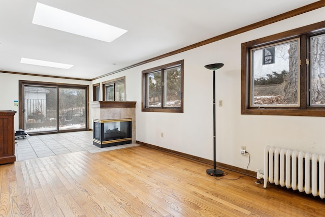 unfurnished living room with radiator, crown molding, light hardwood / wood-style flooring, a skylight, and a multi sided fireplace