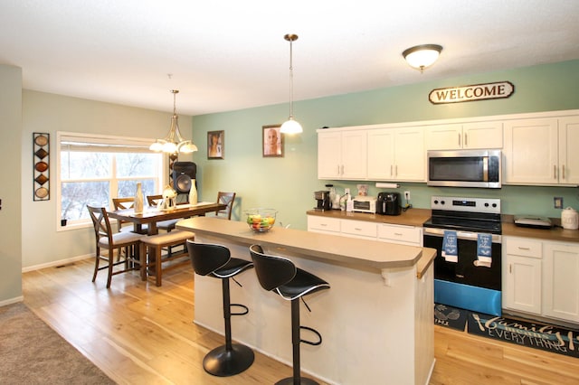 kitchen featuring white cabinetry, stainless steel appliances, decorative light fixtures, and light wood-type flooring