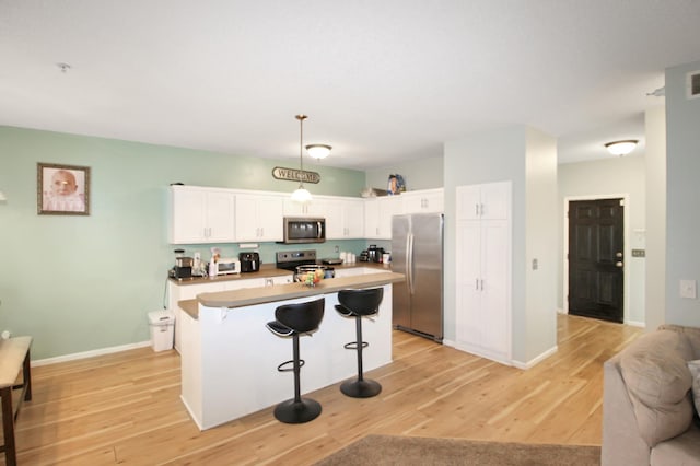 kitchen featuring light hardwood / wood-style floors, white cabinetry, stainless steel appliances, and hanging light fixtures