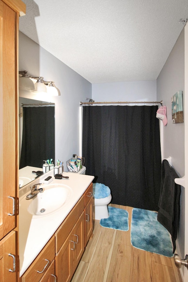 bathroom featuring a shower with shower curtain, vanity, a textured ceiling, hardwood / wood-style floors, and toilet