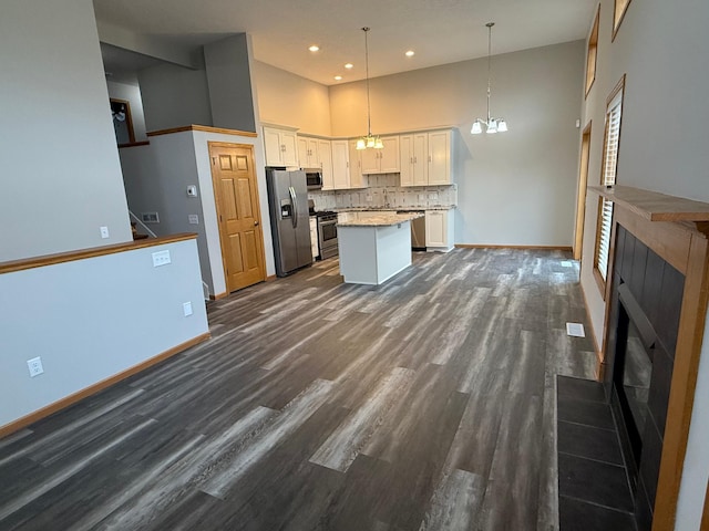 kitchen featuring a center island, stainless steel appliances, a high ceiling, decorative light fixtures, and white cabinets