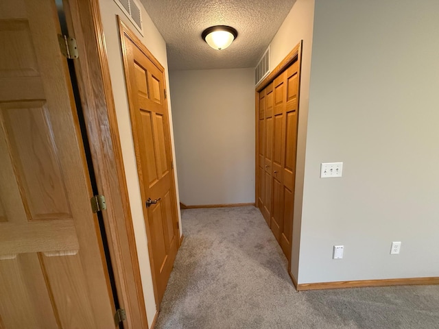 hallway with a textured ceiling and light carpet