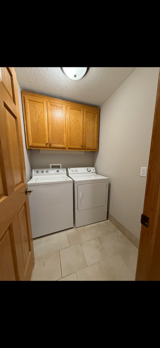 laundry room featuring light tile patterned floors, cabinets, a textured ceiling, and independent washer and dryer