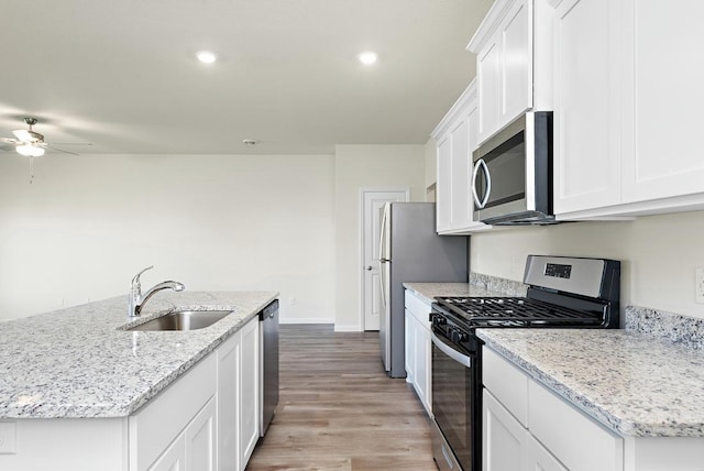 kitchen with appliances with stainless steel finishes, light wood-type flooring, a kitchen island with sink, sink, and white cabinetry