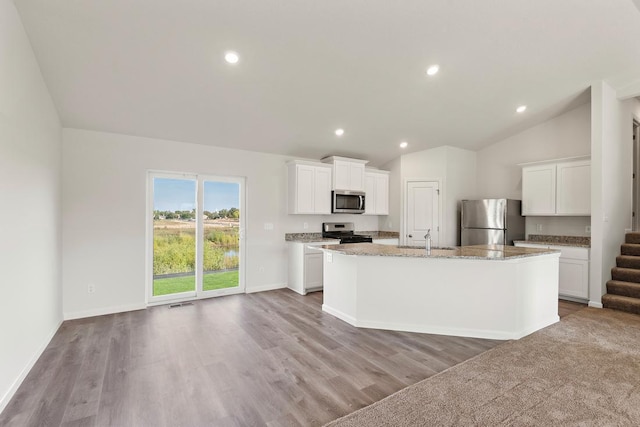 kitchen with lofted ceiling, a center island with sink, white cabinets, light wood-type flooring, and stainless steel appliances