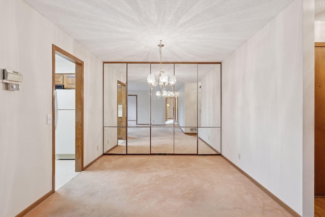 spare room with a textured ceiling, a notable chandelier, and light carpet