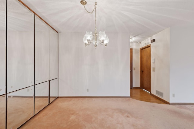 empty room featuring light carpet and a chandelier