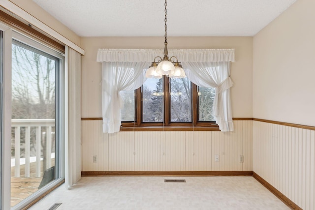 unfurnished dining area with carpet flooring, a textured ceiling, and a notable chandelier