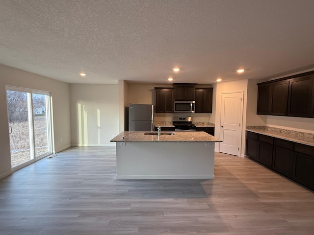 kitchen with dark brown cabinetry, stainless steel appliances, light hardwood / wood-style flooring, an island with sink, and a textured ceiling