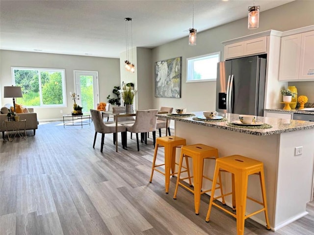 kitchen with decorative light fixtures, white cabinetry, stainless steel fridge, a kitchen breakfast bar, and light stone countertops