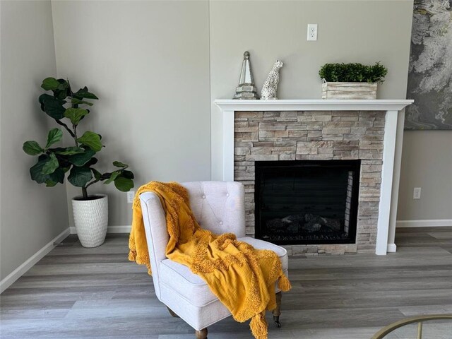 sitting room with baseboards, wood finished floors, and a stone fireplace