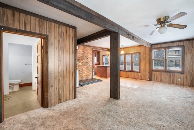 unfurnished living room featuring ceiling fan, beamed ceiling, brick wall, wood walls, and light carpet