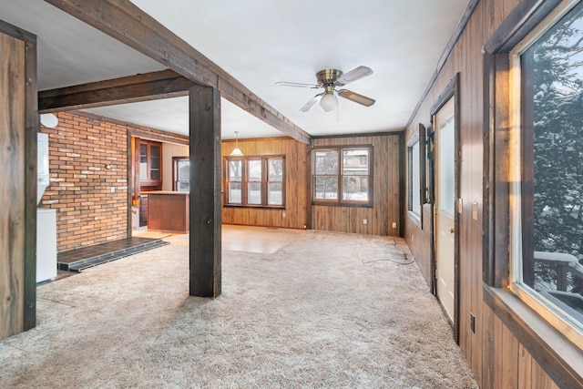 interior space with light carpet, brick wall, ceiling fan, wooden walls, and beam ceiling