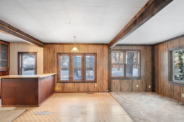 unfurnished dining area with wood walls, beam ceiling, and light colored carpet