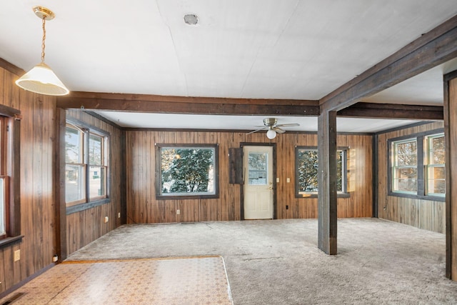 interior space with ceiling fan, wooden walls, and beamed ceiling