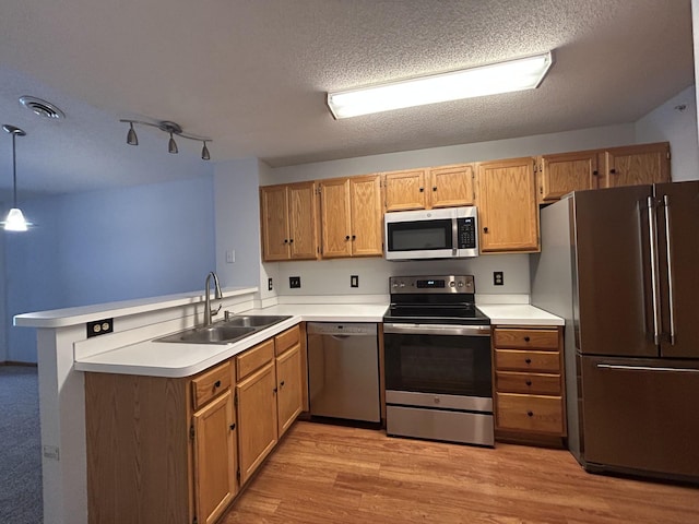 kitchen featuring sink, stainless steel appliances, light hardwood / wood-style flooring, kitchen peninsula, and decorative light fixtures