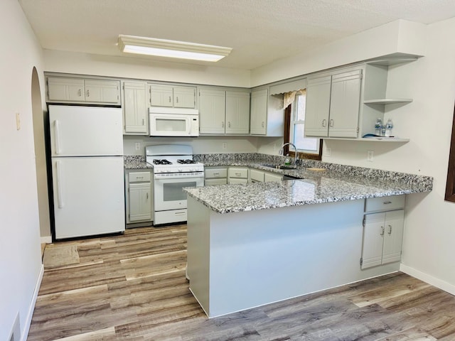 kitchen featuring sink, light stone counters, kitchen peninsula, white appliances, and light wood-type flooring