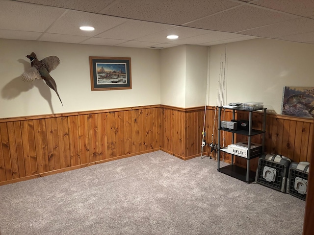 basement featuring carpet, a paneled ceiling, and wooden walls