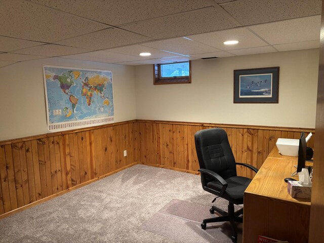 unfurnished office featuring a paneled ceiling, wood walls, and carpet floors
