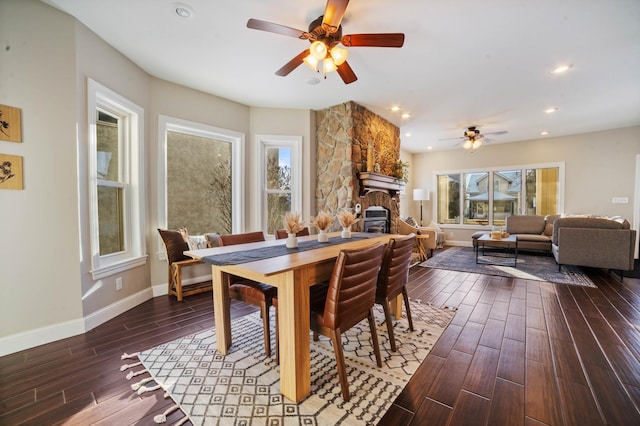 dining room featuring ceiling fan, a stone fireplace, and dark hardwood / wood-style flooring