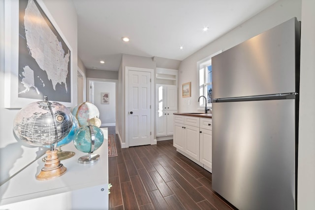 kitchen with white cabinets, dark hardwood / wood-style flooring, stainless steel refrigerator, and sink