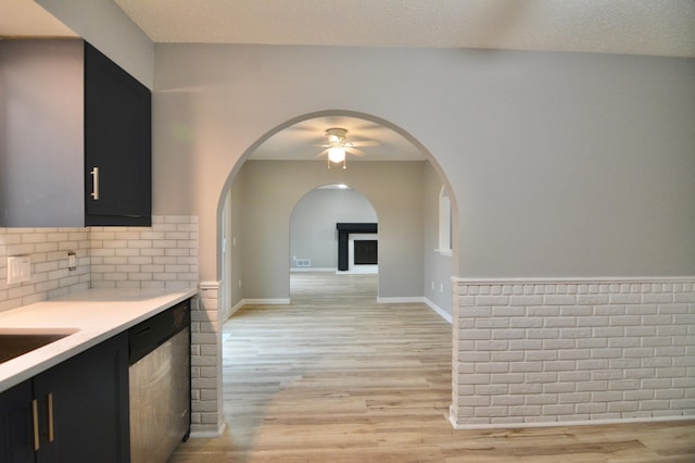 kitchen featuring stainless steel dishwasher, a textured ceiling, ceiling fan, a fireplace, and light hardwood / wood-style floors