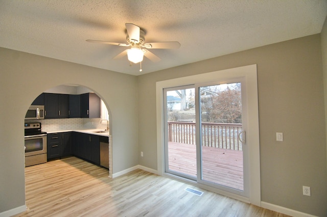 kitchen featuring light wood-type flooring, backsplash, stainless steel appliances, ceiling fan, and sink