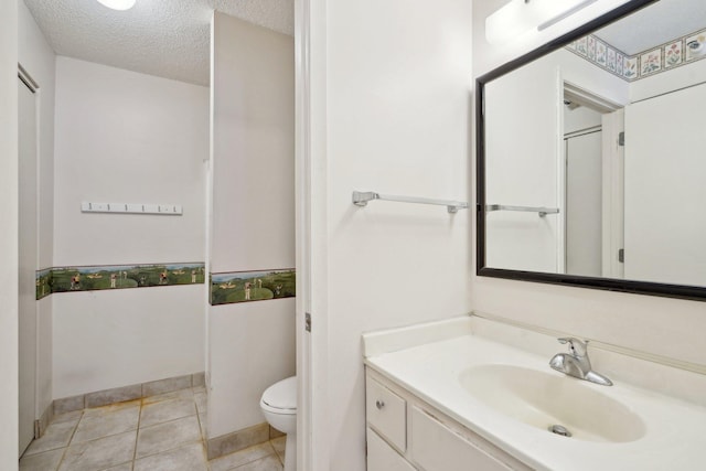 bathroom with tile patterned flooring, vanity, toilet, and a textured ceiling