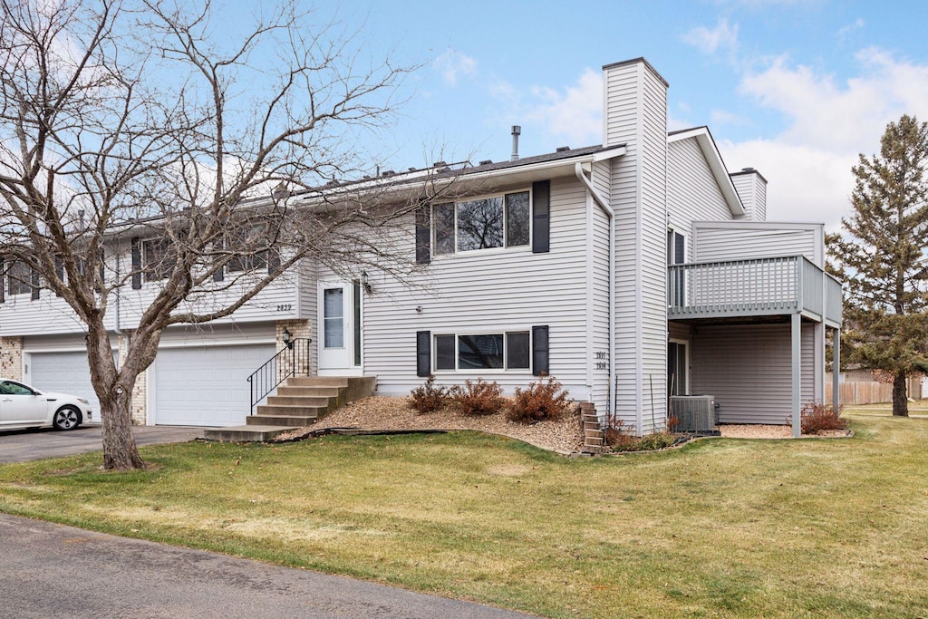 bi-level home with a balcony, central air condition unit, and a front yard