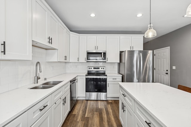 kitchen featuring light stone counters, pendant lighting, appliances with stainless steel finishes, white cabinets, and a sink