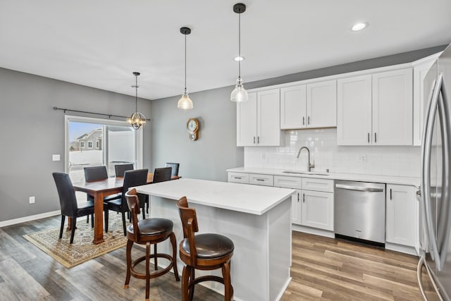 kitchen with a sink, white cabinetry, light countertops, appliances with stainless steel finishes, and hanging light fixtures