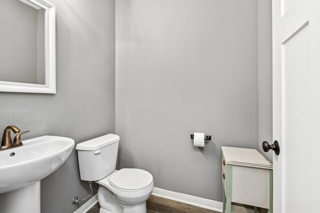 half bathroom featuring a sink, toilet, baseboards, and wood finished floors