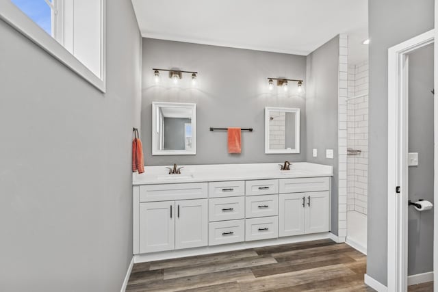 full bath featuring double vanity, wood finished floors, a sink, and baseboards