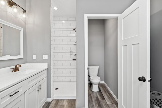 bathroom with toilet, vanity, a shower stall, wood finished floors, and baseboards