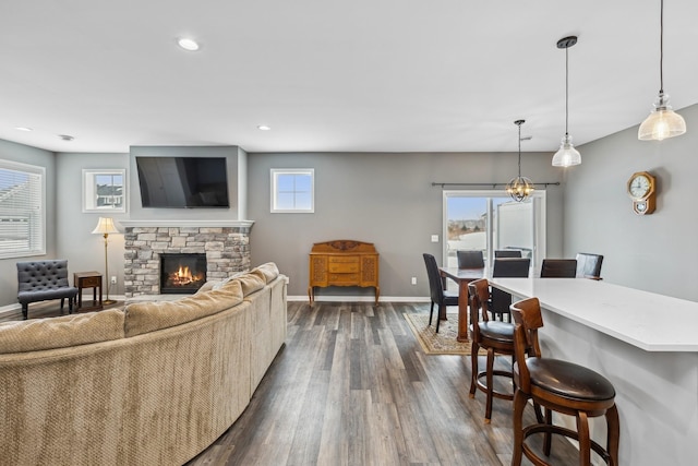 living room featuring dark wood finished floors, recessed lighting, a stone fireplace, a chandelier, and baseboards