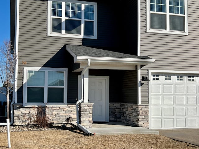 doorway to property featuring a garage, stone siding, and roof with shingles