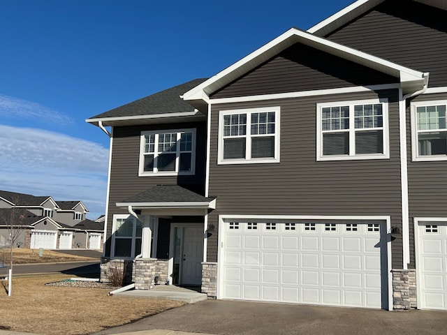 view of front of house featuring a garage, stone siding, aphalt driveway, and roof with shingles