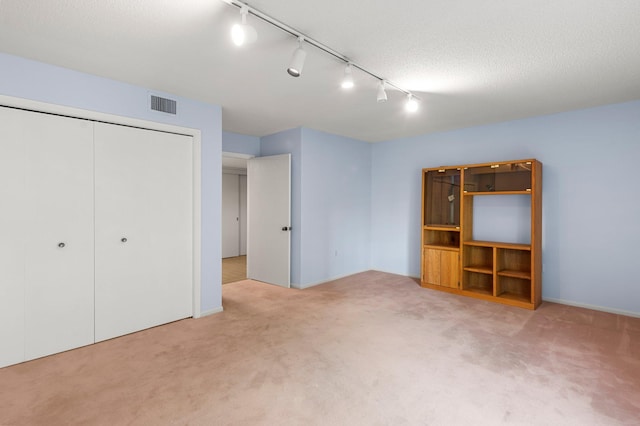 unfurnished bedroom with light carpet, a textured ceiling, track lighting, and a closet