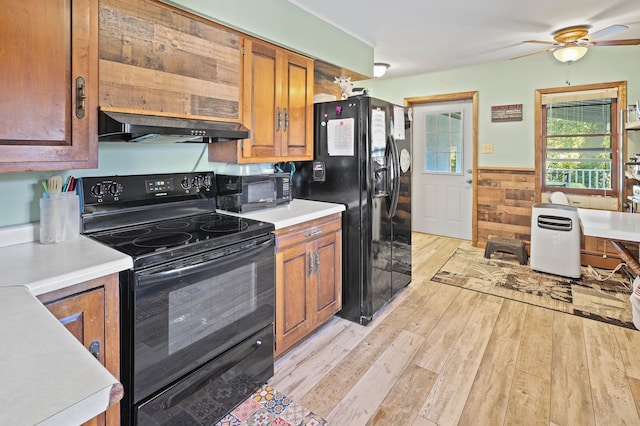 kitchen featuring black appliances, wooden walls, ceiling fan, light wood-type flooring, and range hood