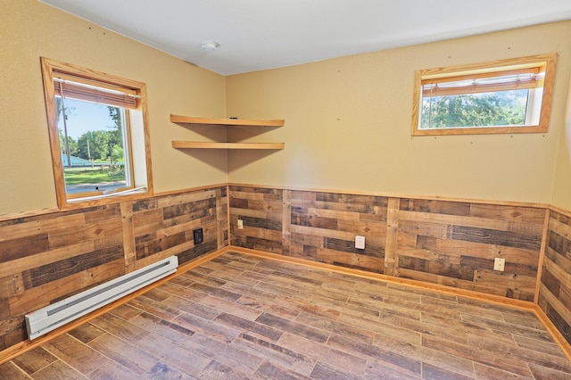 empty room featuring a healthy amount of sunlight, wooden walls, a baseboard heating unit, and wood-type flooring