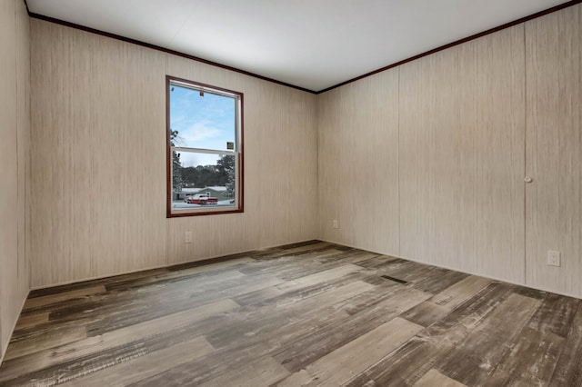 unfurnished room featuring wood walls, light wood-type flooring, and crown molding