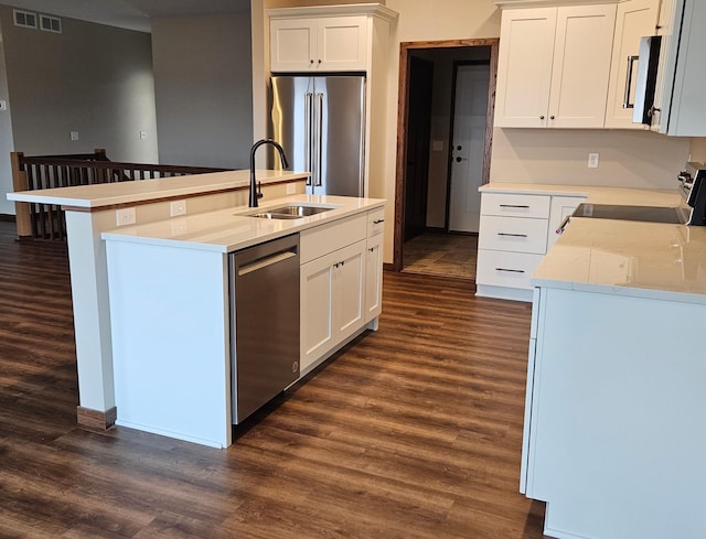 kitchen with appliances with stainless steel finishes, white cabinets, dark hardwood / wood-style flooring, sink, and a kitchen island with sink