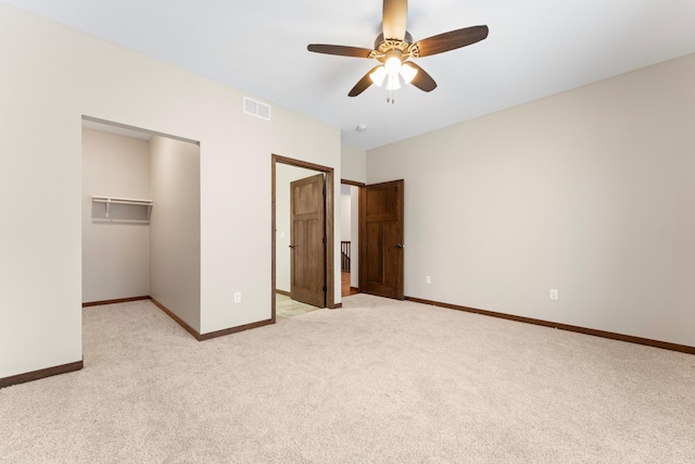 unfurnished bedroom featuring ceiling fan, a closet, a walk in closet, and light colored carpet