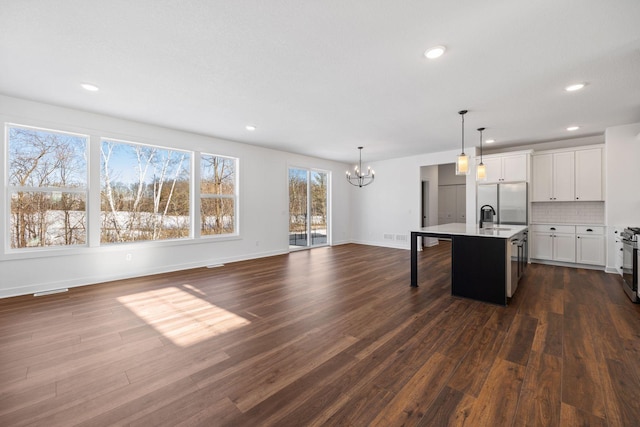 kitchen featuring a kitchen island with sink, a chandelier, hanging light fixtures, decorative backsplash, and sink